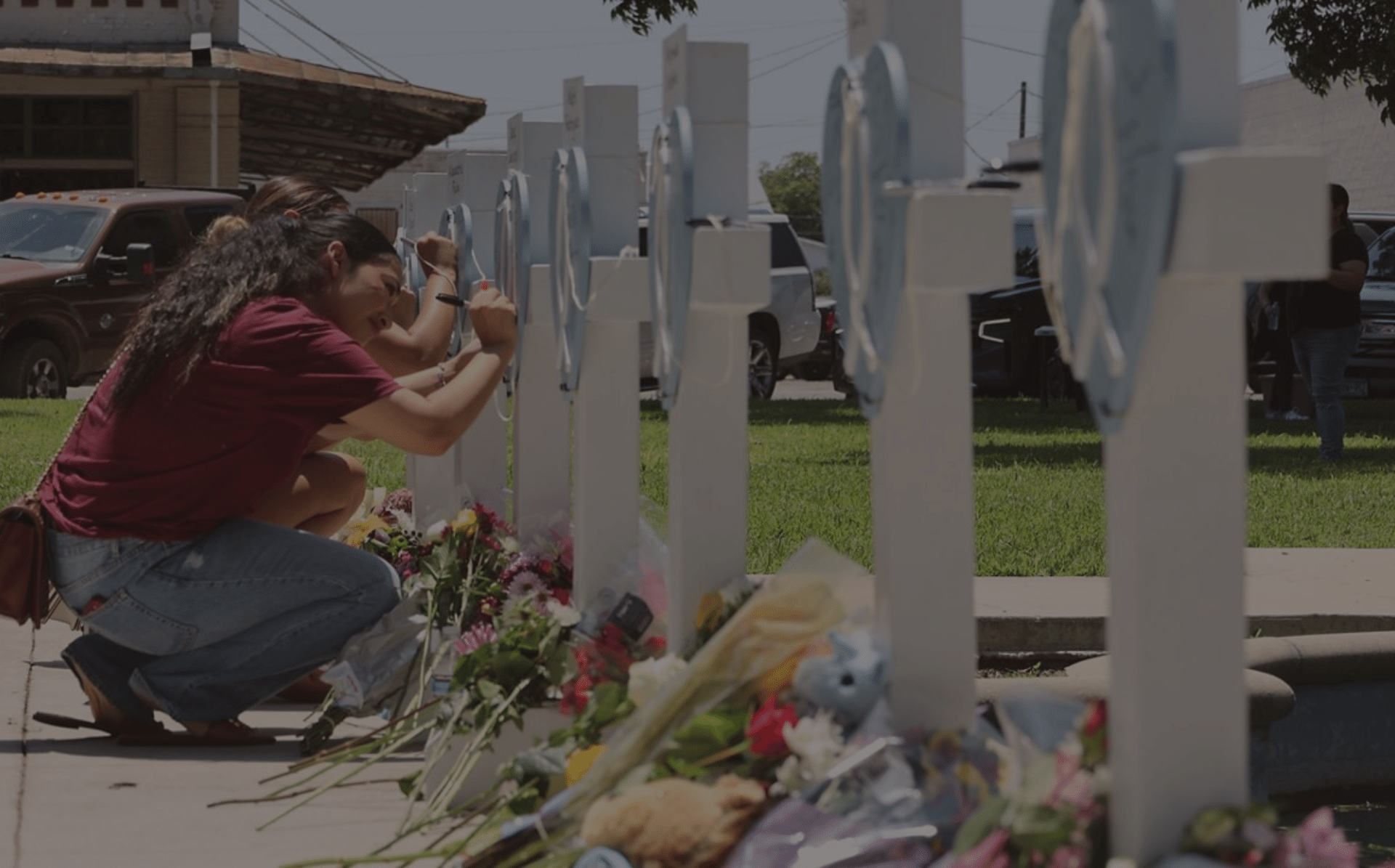 Women leaning to sign crosses set at Uvalde memorial for victims of gun violence