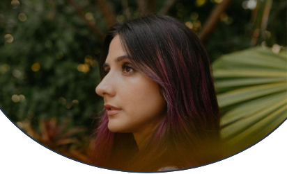 Profile photo of disability activist and model Paula Carozzo facing left with a background of trees and palm trees