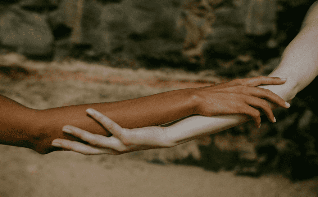 A brown skinned arm and a white skinned arm holding arms in the outdoors