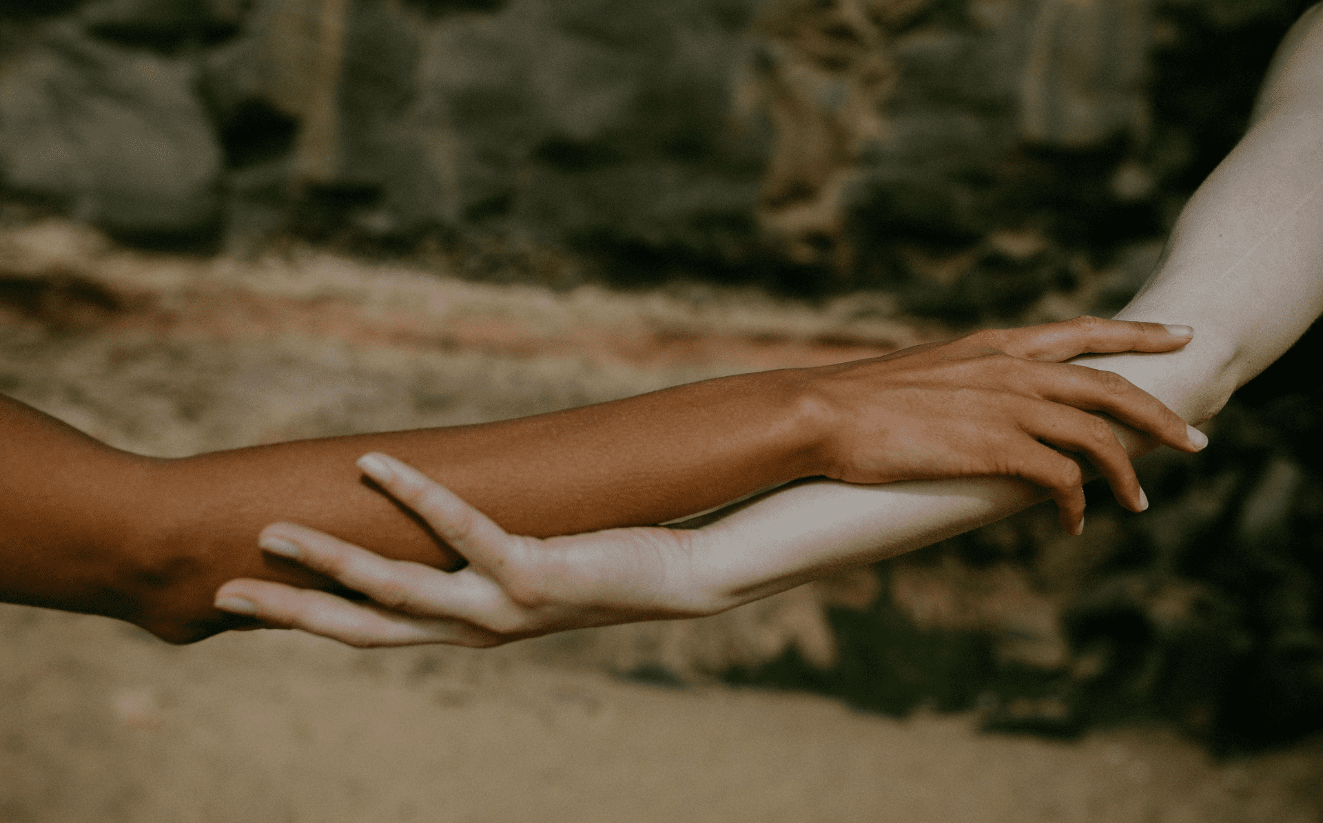 A brown skinned arm and a white skinned arm holding arms in the outdoors