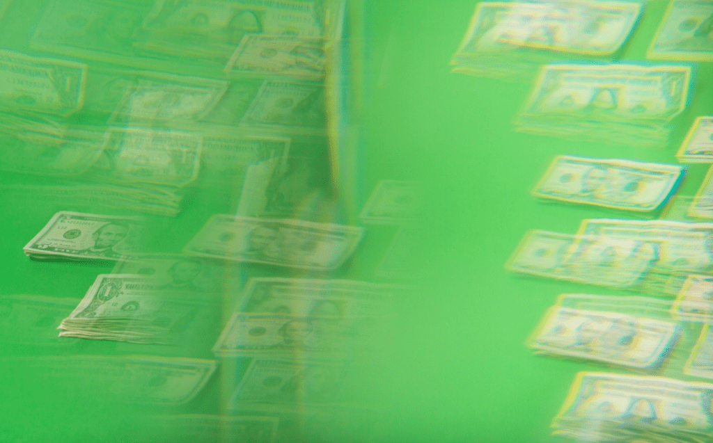 This is a off-focus picture of stacks of money on a green background that was taken through a kaleidoscope lens. 