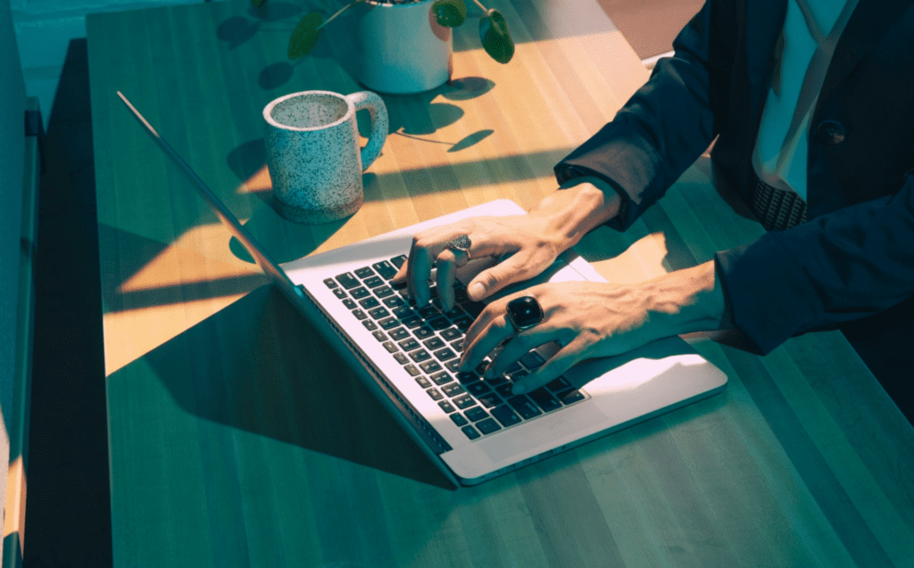 Woman's hands on a laptop keyboard, with a coffee mug on her right