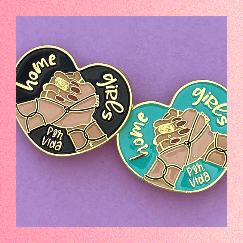 Two heart shaped pins that say "Home girls por vida" with two manicured hands doing a shake from Ex-Voto Designs shown as a Galentine's Day or Valentine's Day gift