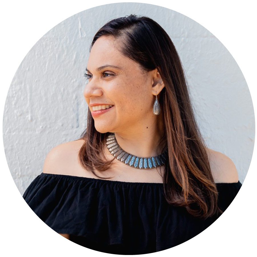 Wendy Amara is pictured wearing a Black shoulder top with a bronze necklace and matching earings. She is smiling facing left, so we see her profile. Her straight hair is down with a side part. 